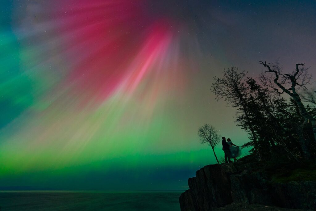 Engaged couple holding hands under glowing Northern Lights in North Shore, Minnesota
