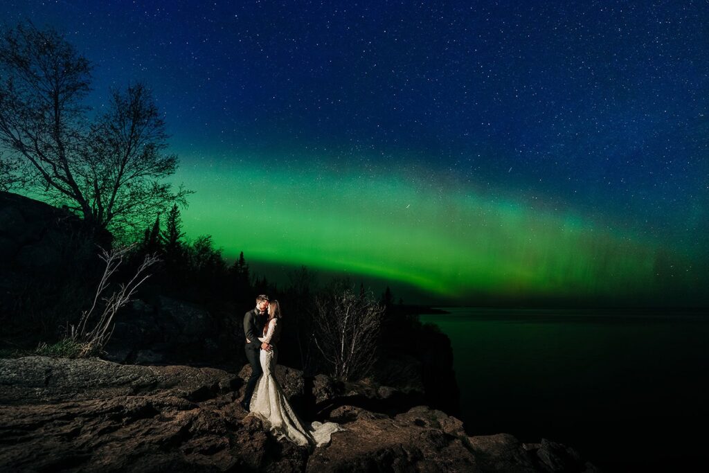Wedding couple embracing beneath green aurora borealis on the North Shore, MN