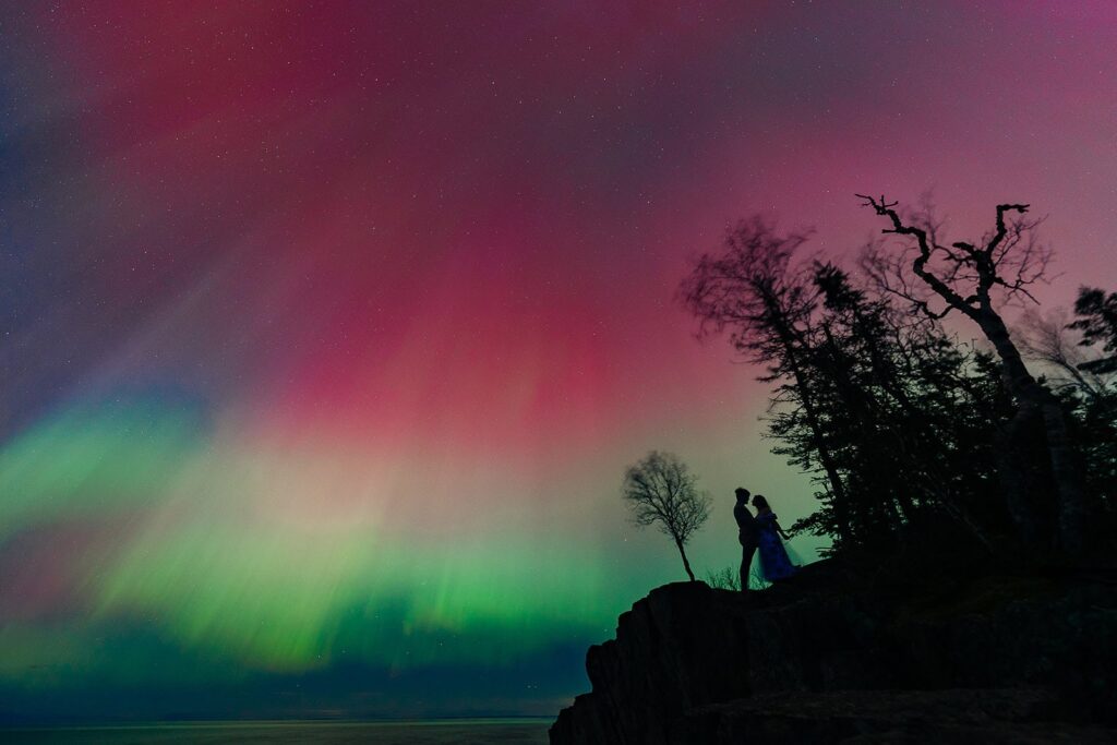 Adventurous couple posing under Northern Lights on rocky shoreline in North Shore, MN