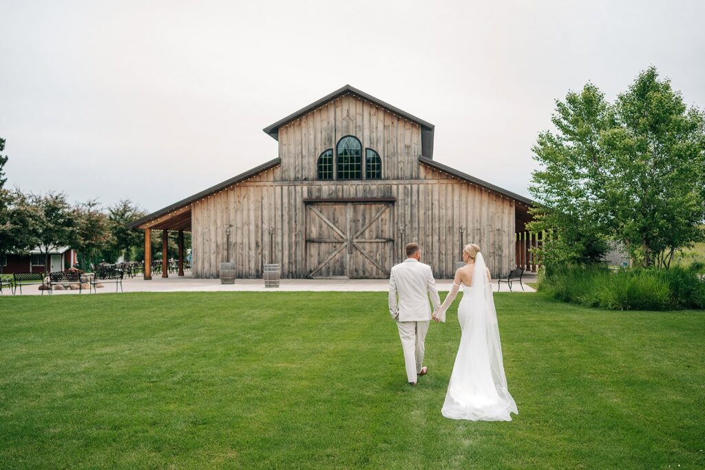 Bride and groom walking hand in hand towards creekside farm wedding venue's rustic barn